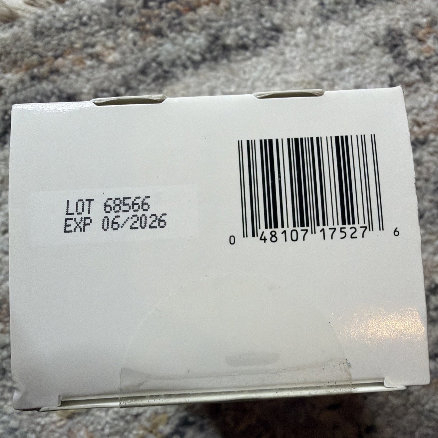 White product box showing a barcode and a printed label with lot number 68566 and expiration date of June 2026 on a textured surface.