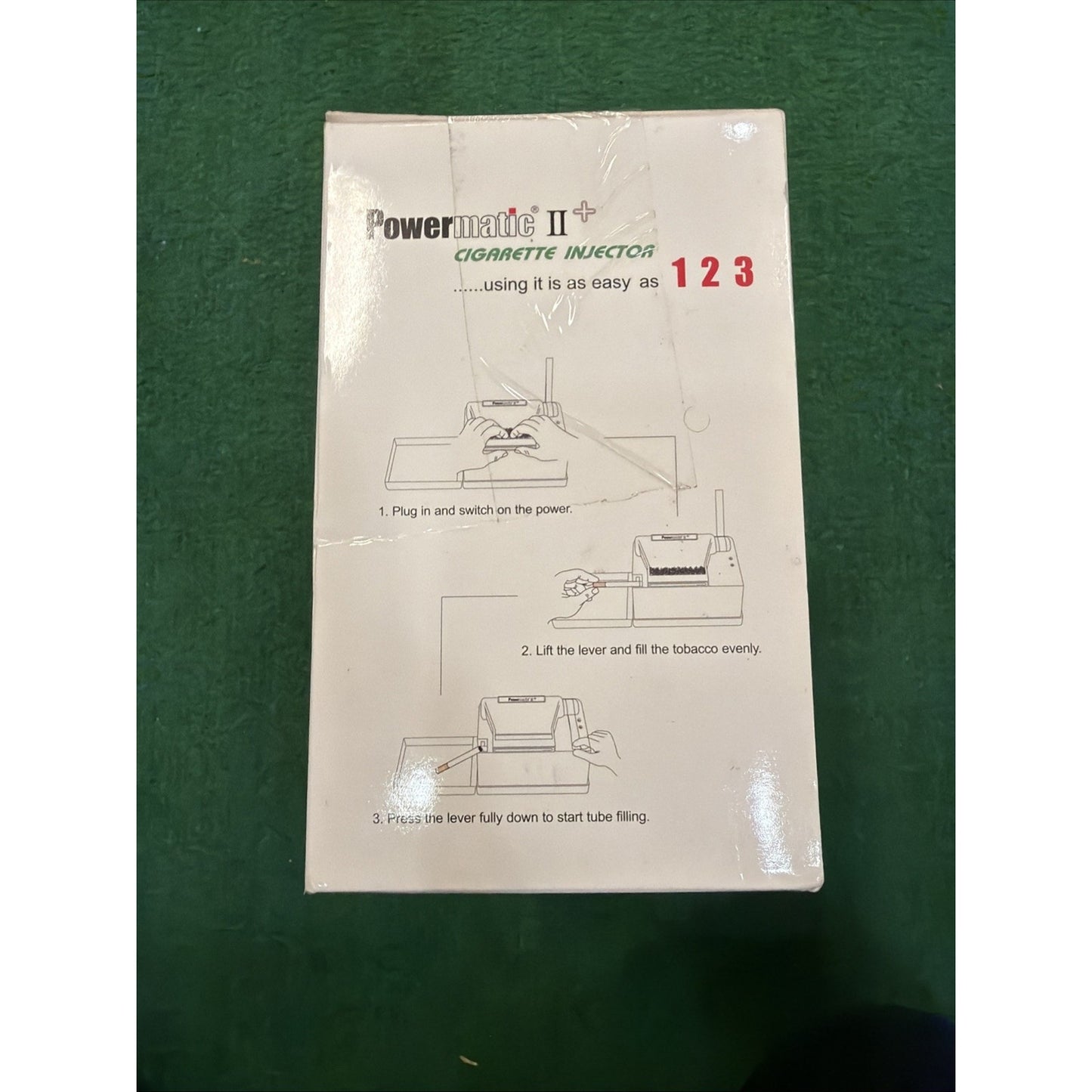 White product box featuring printed instructions and simple line drawings demonstrating the three-step process to use a Powermatic II+ cigarette injector machine.