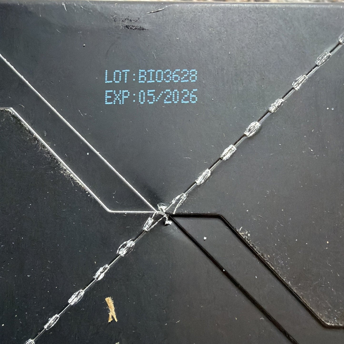 Close-up of black packaging showing printed lot number BI03628 and expiration date 05/2026 with visible embossed seam details.