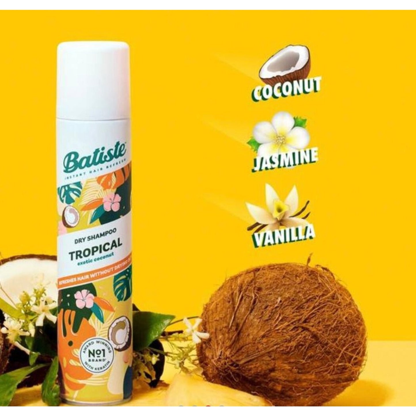 Can of Batiste Tropical dry shampoo with colorful tropical floral and coconut illustrations, displayed next to a whole coconut and flower blossoms on a bright yellow background.