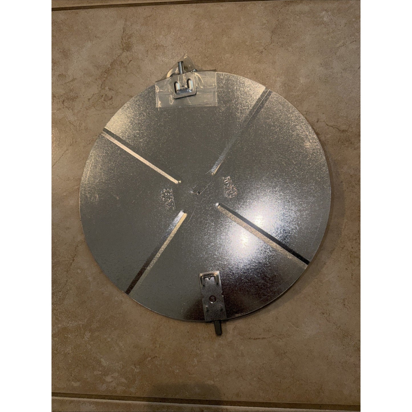 Round galvanized metal reflector with three evenly spaced slotted openings and two adjustable mounting brackets on a beige stone surface.