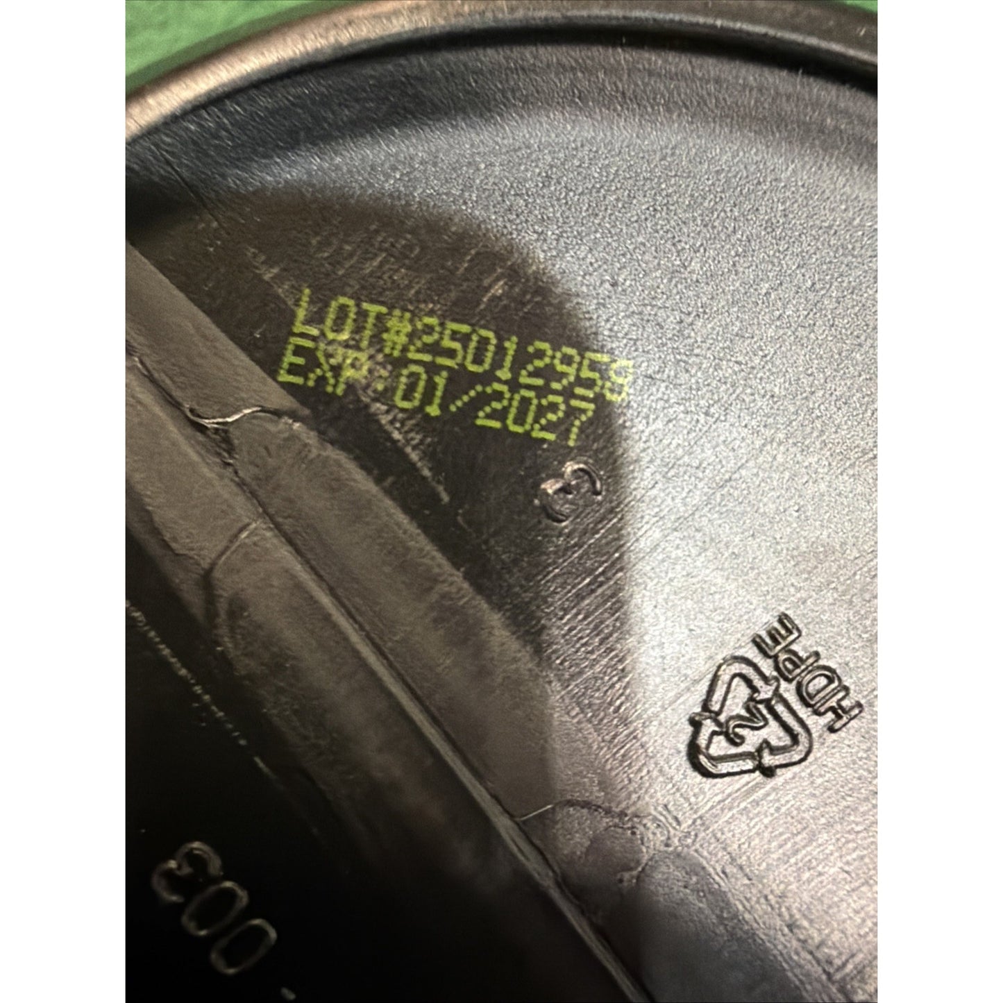 Close-up of a black plastic container lid showing a yellow printed lot number and expiration date, with a recycling symbol indicating HDPE material.
