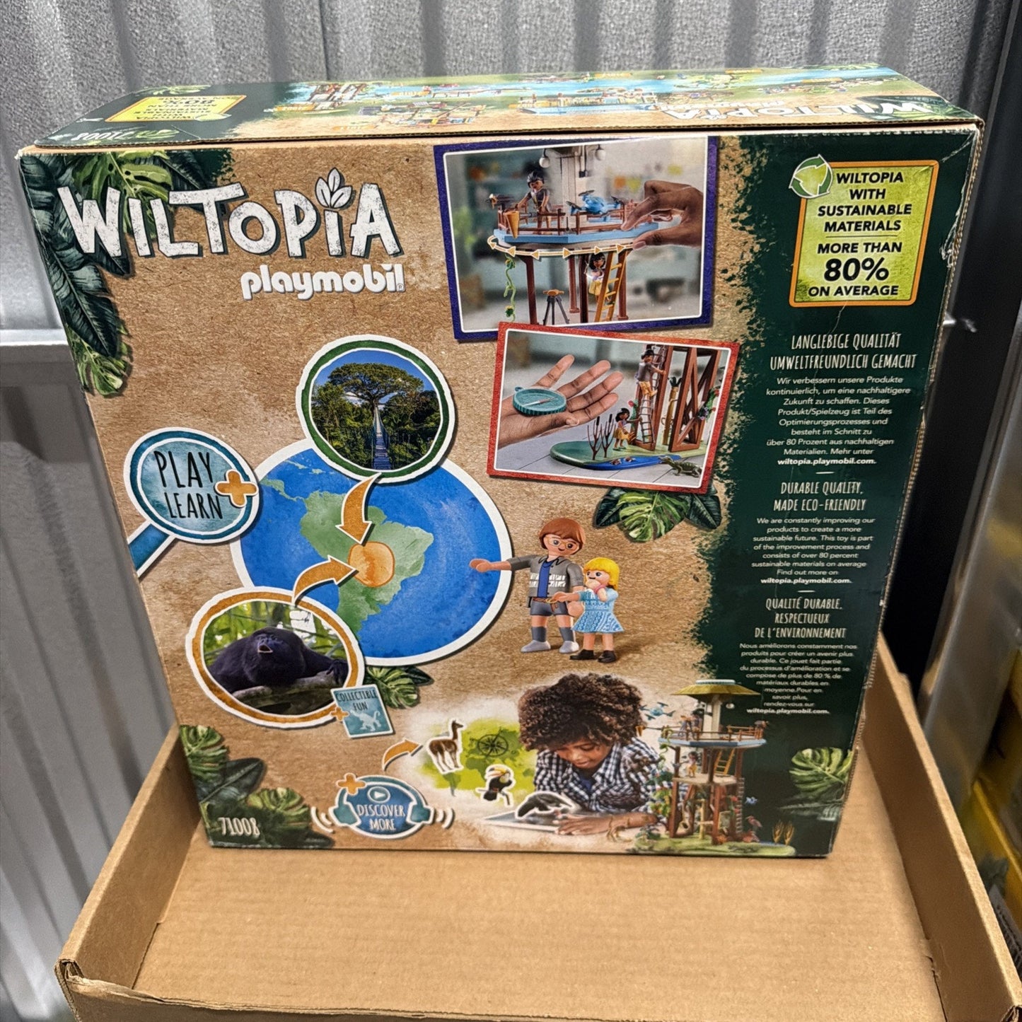 Back of a Playmobil Wiltopia box featuring images of children playing with eco-friendly toy sets, a globe highlighting rainforest conservation, and text about sustainability and environmental quality.