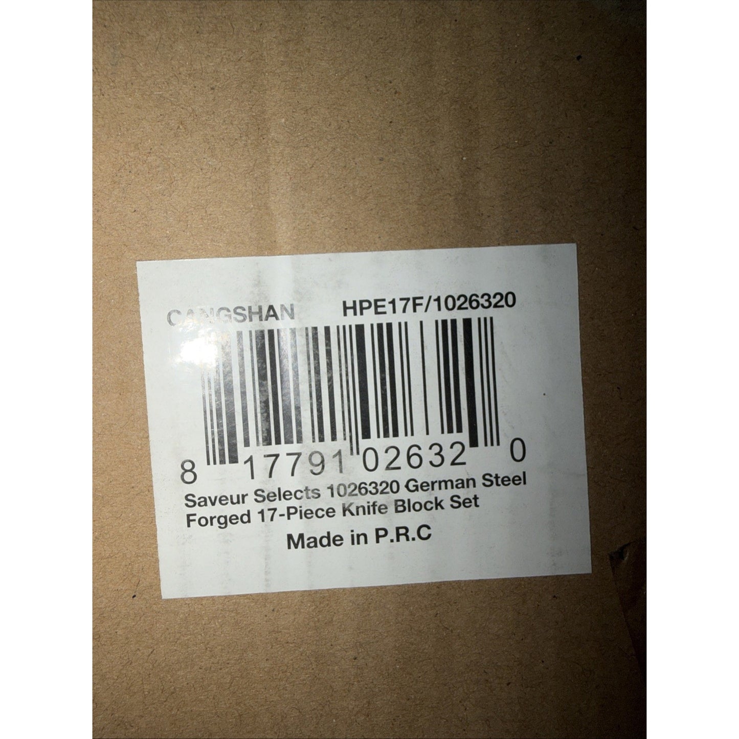 Close-up of a white product label on brown cardboard packaging showing a barcode and text listing a 17-piece German steel forged knife block set made in P.R.C.