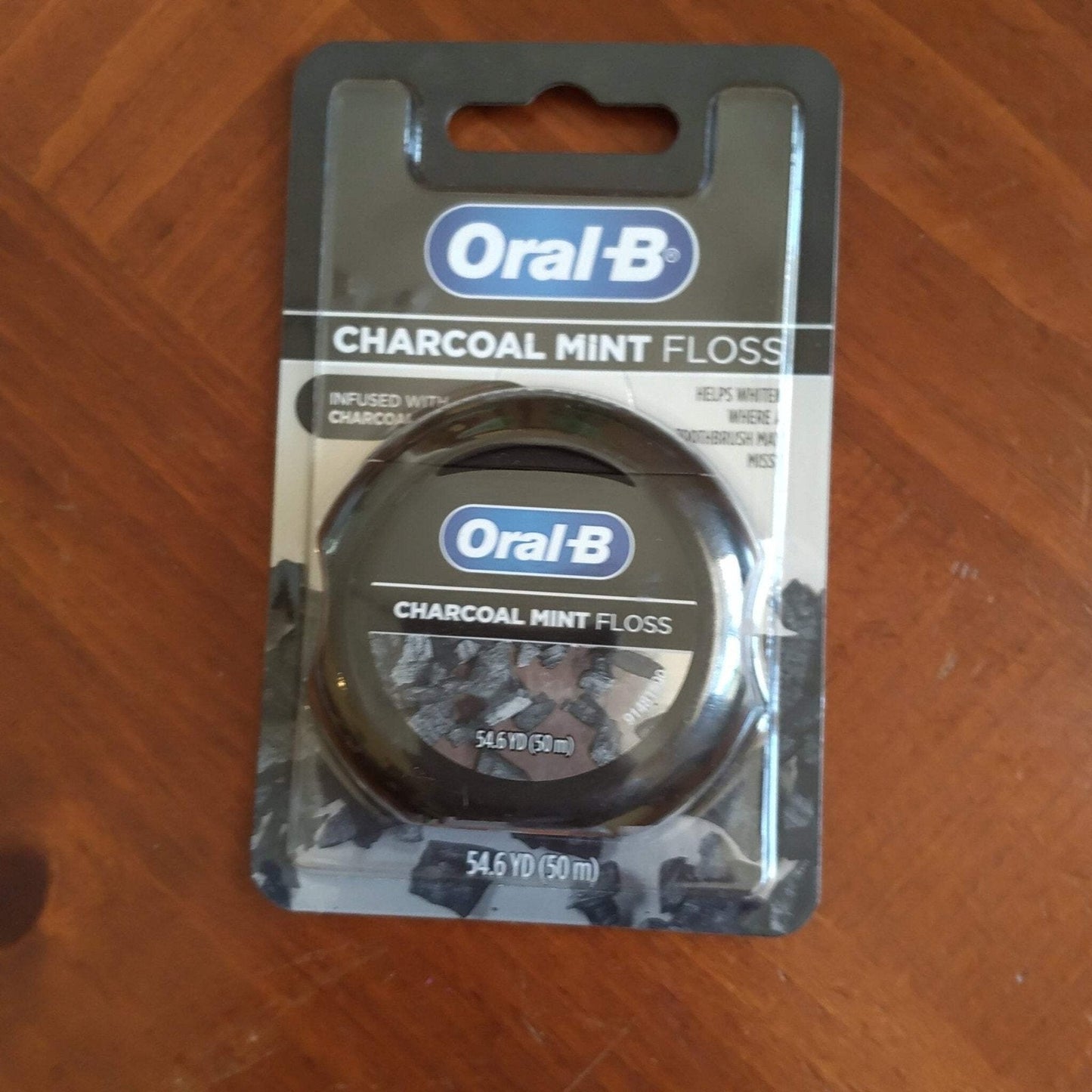 Oral-B Charcoal Mint dental floss in black plastic circular case with a label featuring charcoal imagery and containing 54.6 yards (50 meters) of floss, packaged on a black and gray backing card.