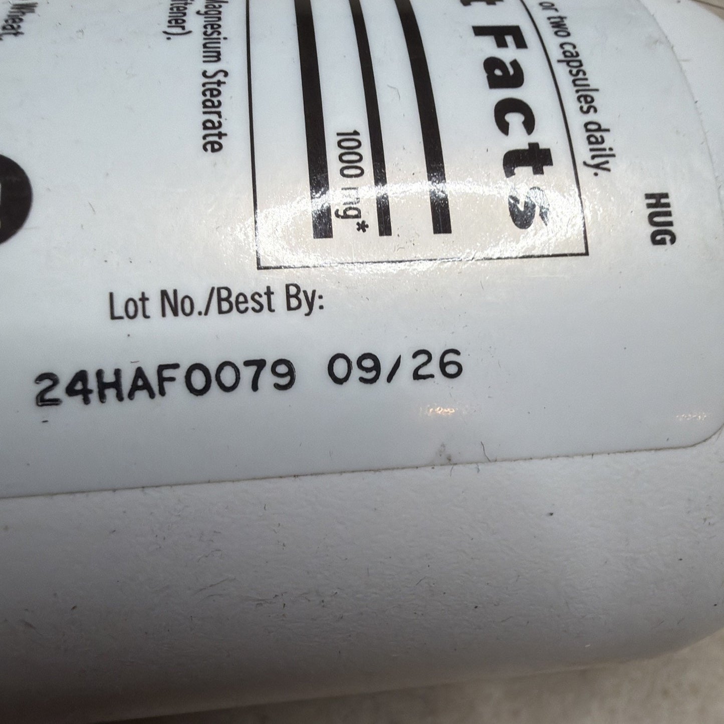 Close-up of a white supplement bottle label showing a lot number and expiration date printed in black ink, with partial nutritional facts and ingredient information visible.