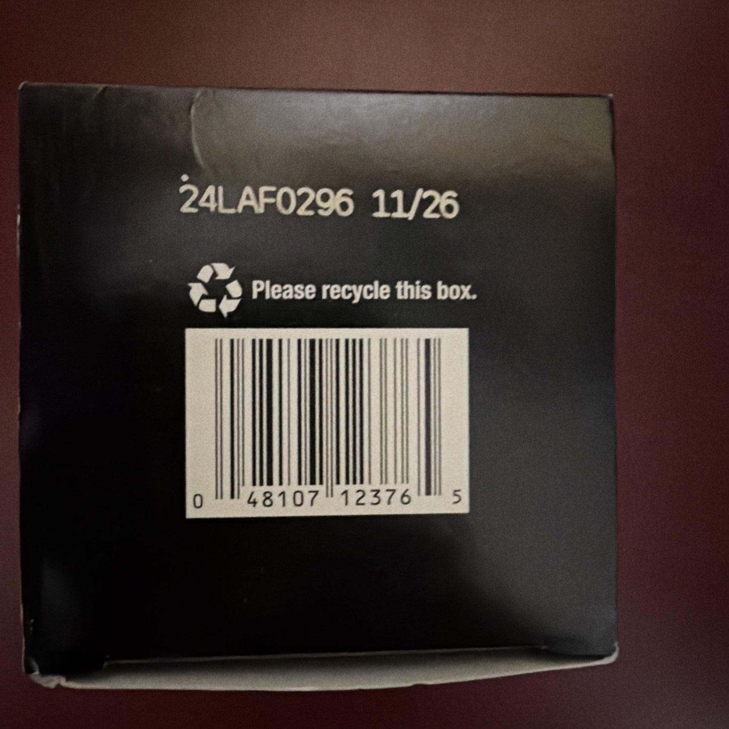 Close-up of a black box showing a printed code "24LAF0296 11/26," a recycling symbol with the message "Please recycle this box," and a barcode with numbers 048107123765.