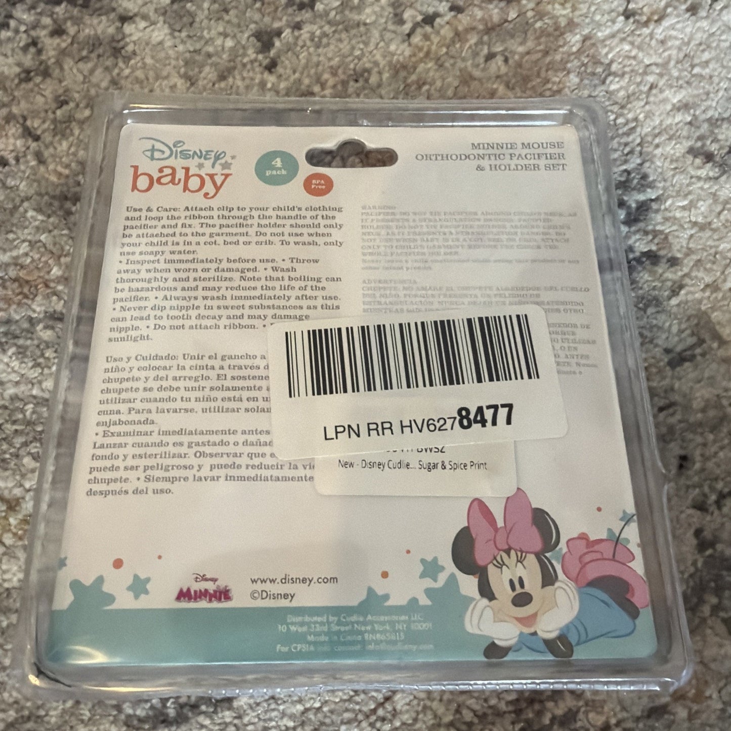 Plastic blister packaging for a Disney Baby Minnie Mouse orthodontic pacifier and holder set, featuring care instructions and a playful Minnie Mouse illustration on the backing card, placed on a carpeted surface.