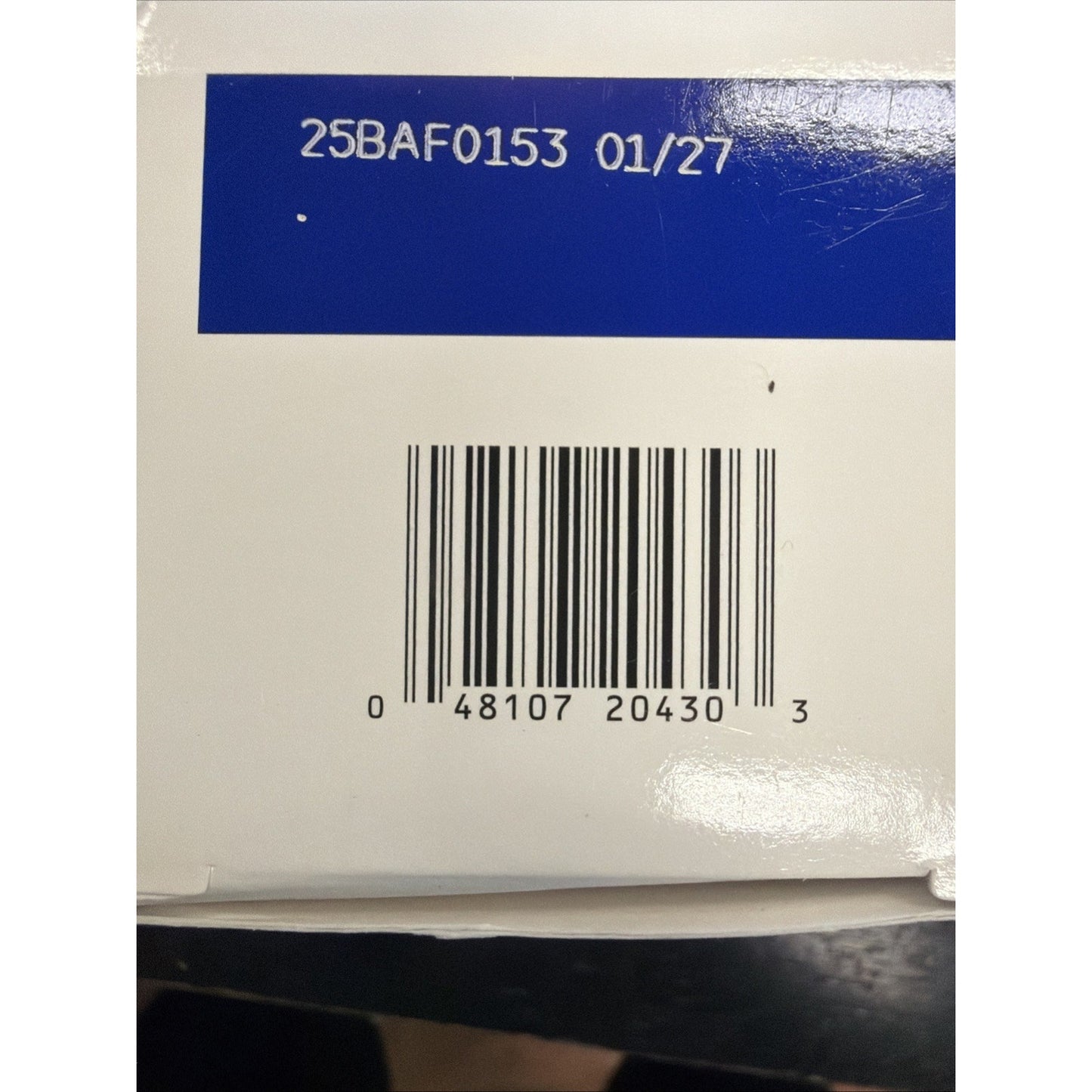 Close-up of a product box showing a barcode with numbers beneath and a printed lot code and expiration date above on a white and blue background.