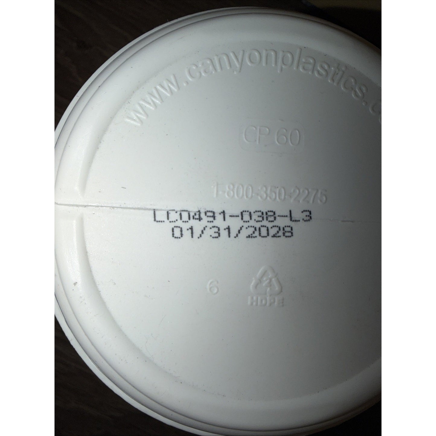 Close-up of a white plastic container lid showing embossed website, contact number, product code, expiration date, and recycling symbol for HDPE material.