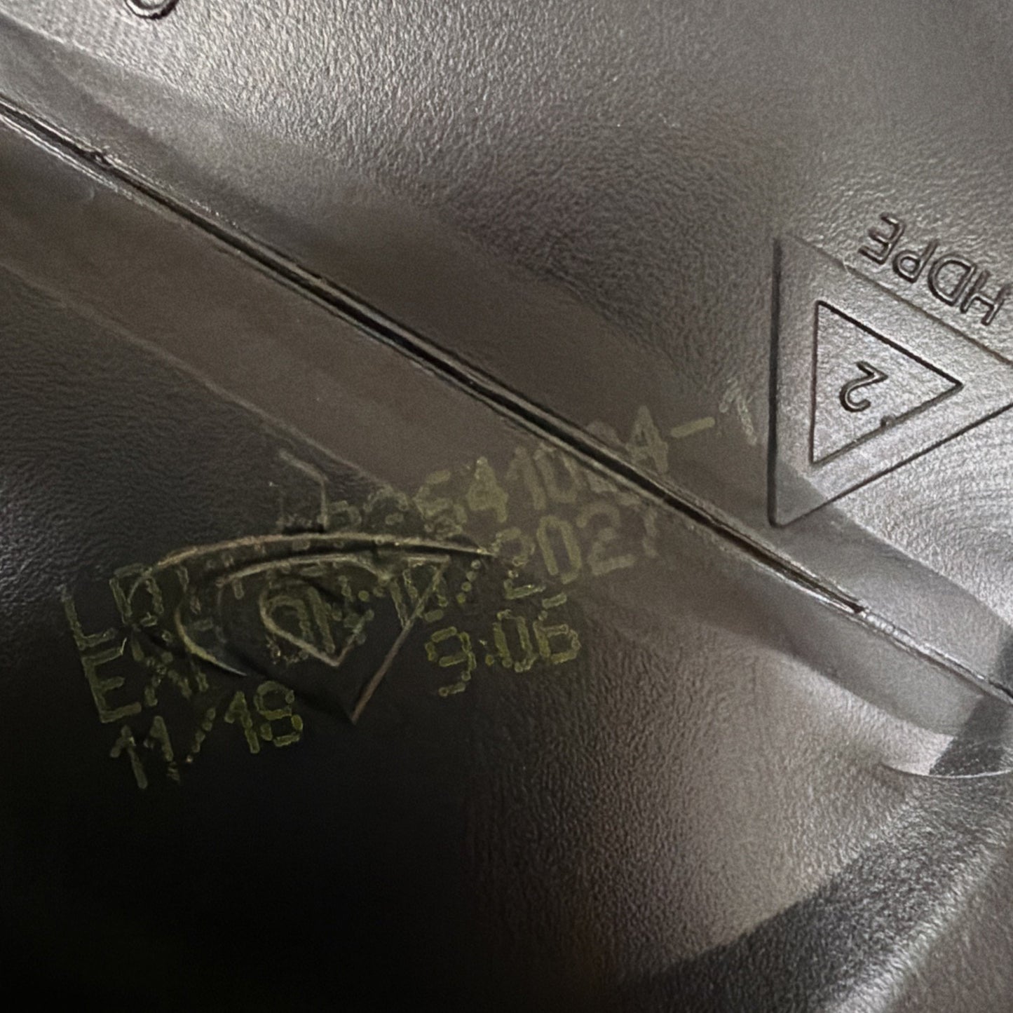 Close-up of a black plastic surface showing yellow printed lot number, expiration date 11/18/2024, time code 9:06, and an embossed recycling symbol with the code "2" and "HDPE" text.