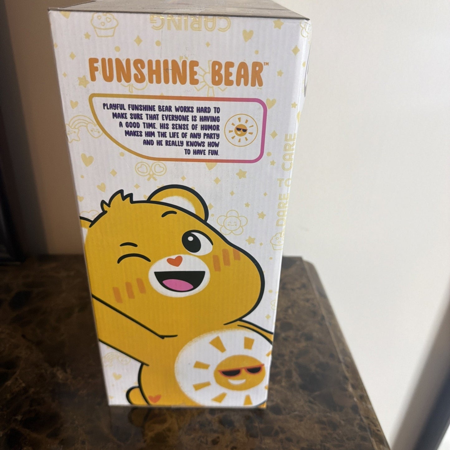 Side view of a Funshine Bear collectible box featuring a cheerful yellow bear winking, with a sun emblem wearing sunglasses on its belly and playful text about the character’s fun-loving personality.