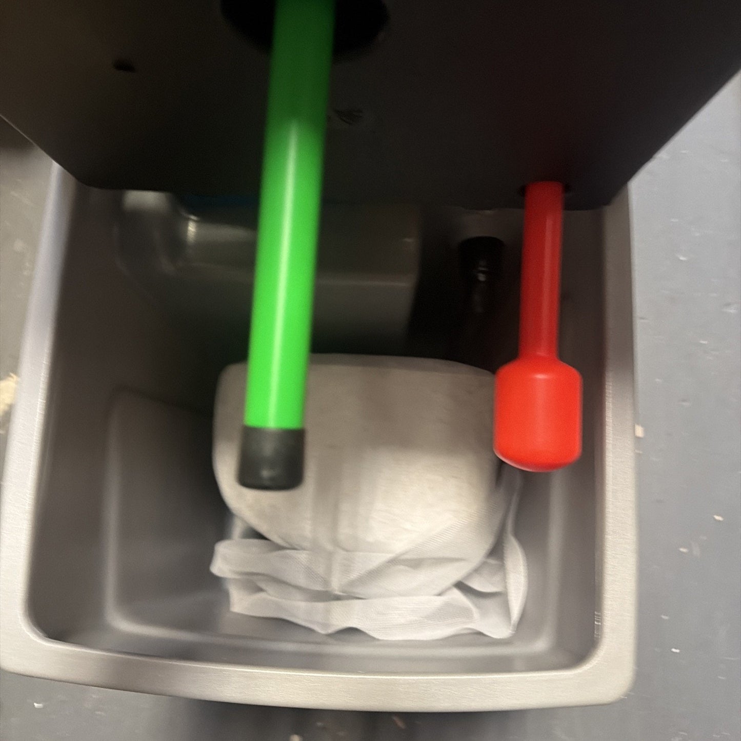 Close-up view of a gray plastic container holding a crumpled white cloth, with two vertically positioned sticks—one green with a black tip and one red with a rounded end—protruding from above.