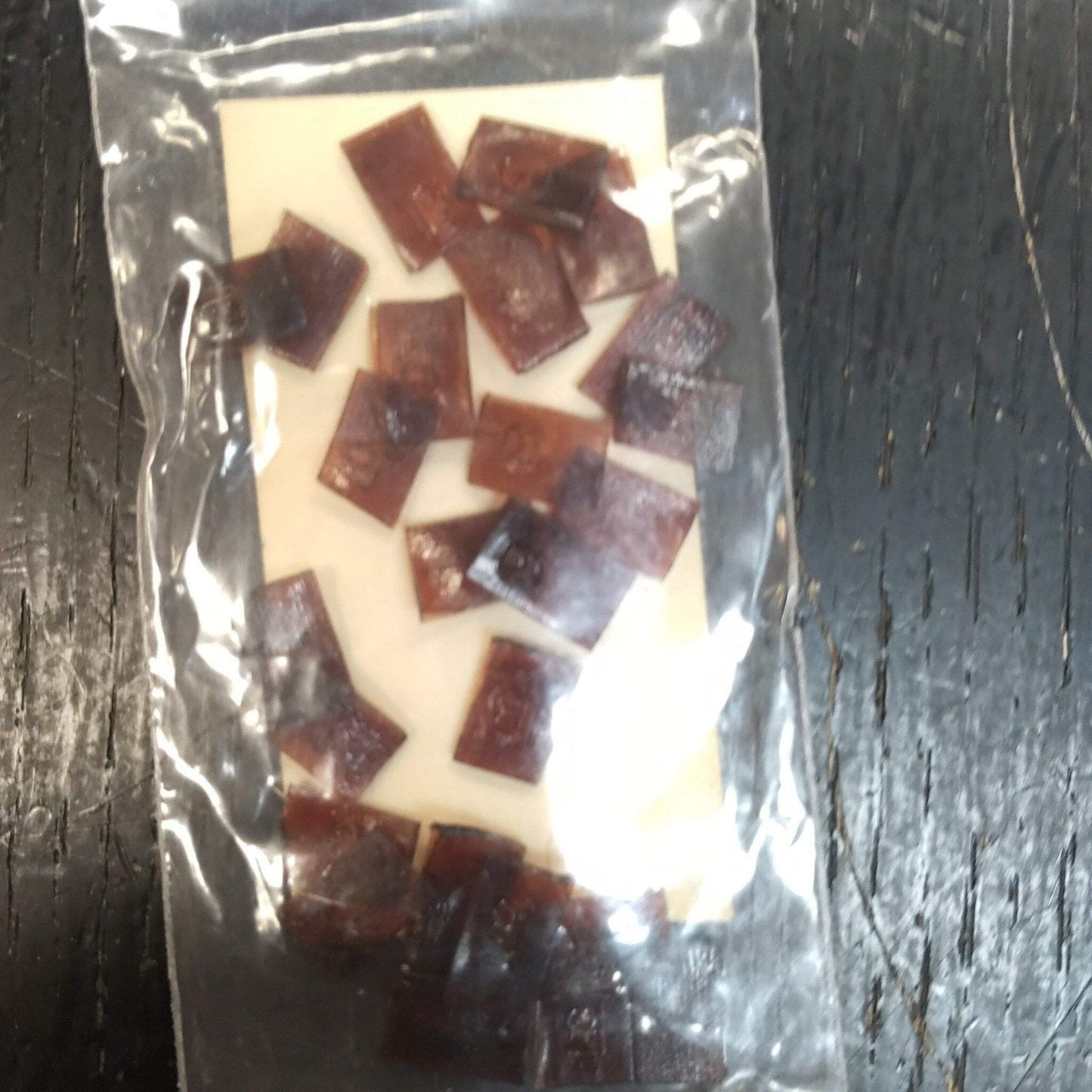 Clear plastic resealable bag containing several small, irregularly shaped dark brown pieces placed on a light-colored card, against a dark wooden surface.
