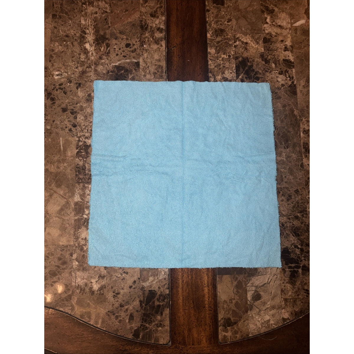 Light blue microfiber cloth laid flat on a polished marble and wood table surface.