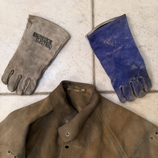 Worn leather welding jacket and two heavy-duty leather welding gloves branded Lincoln Electric and Millitant