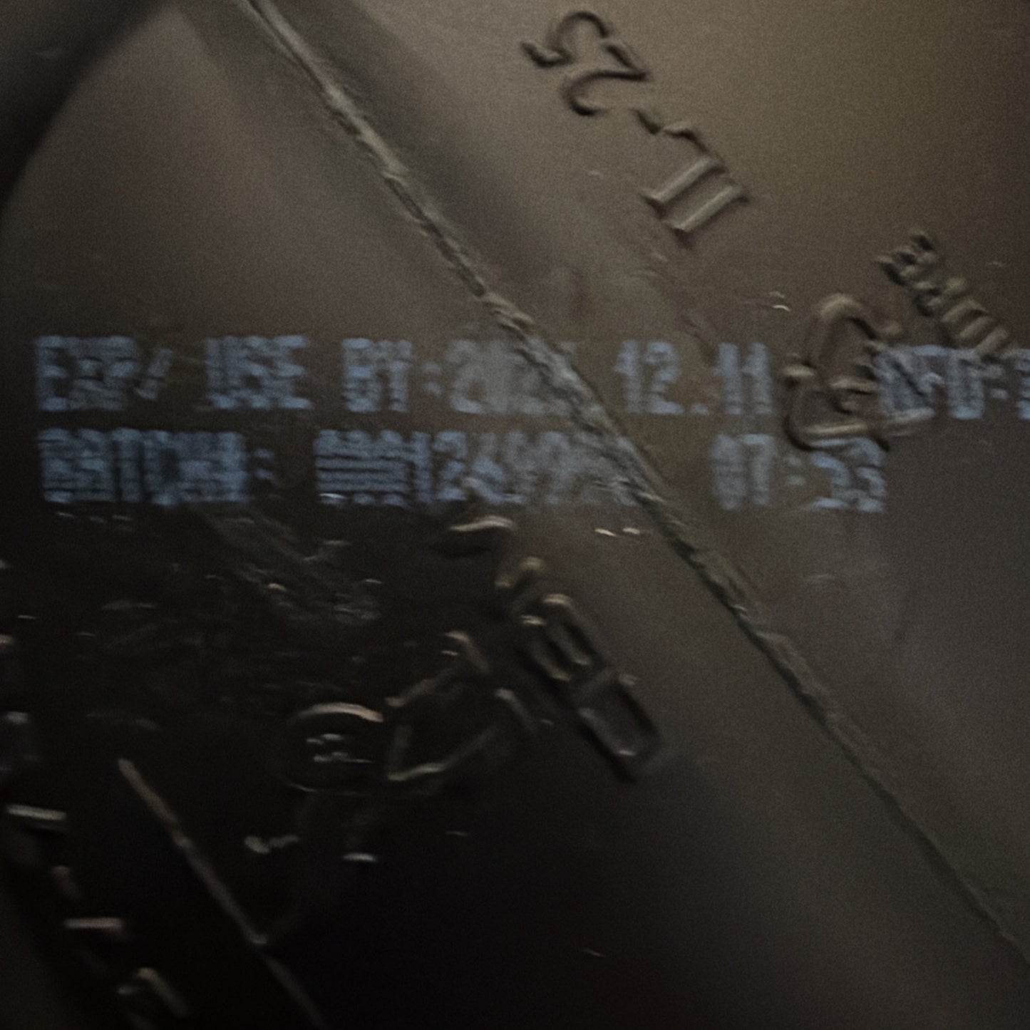 Close-up of a black plastic surface with light blue printed expiration date "2023.12.11" and batch code details, including time stamp "07:53" on a textured background.