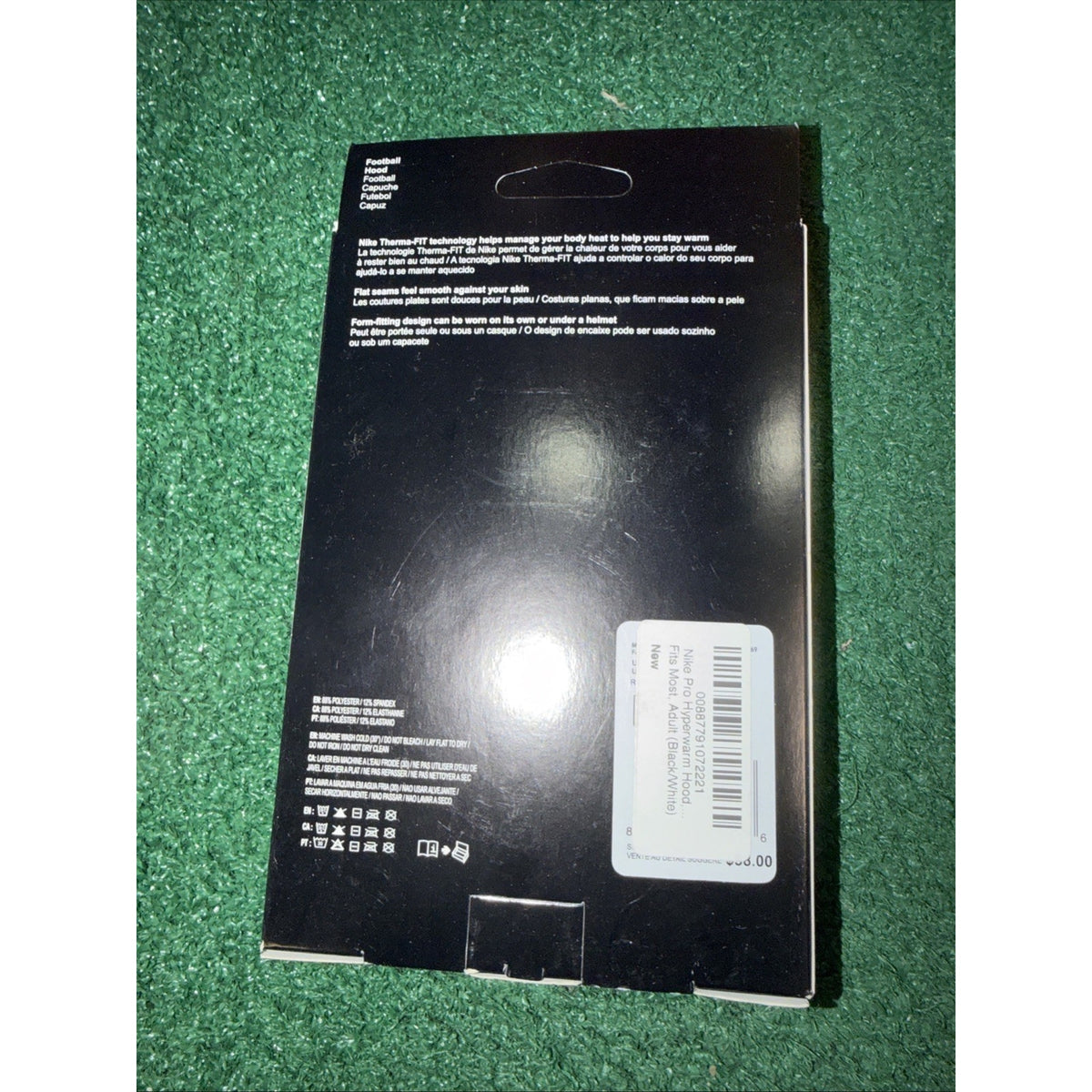 Black rectangular product packaging with white text, a barcode sticker label, and care instructions, placed on a green textured surface.