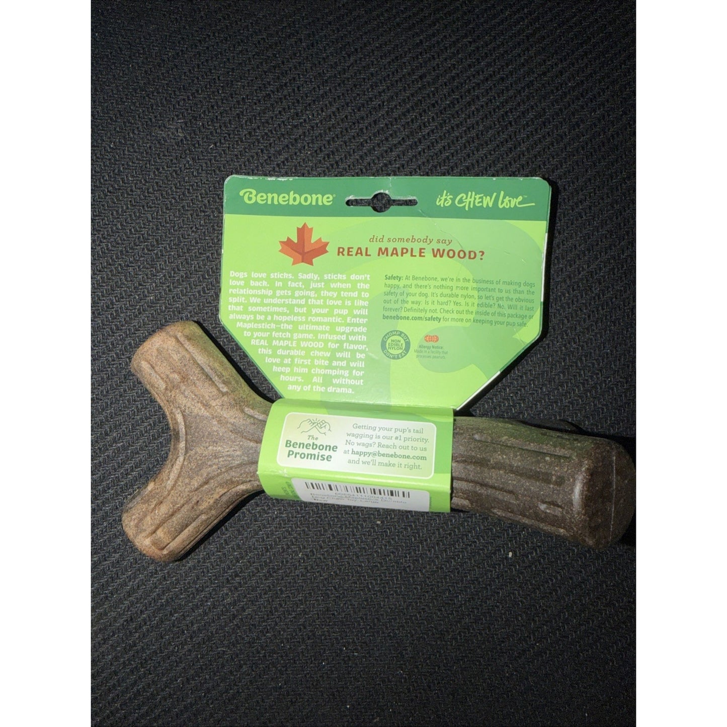 Greenish-brown Y-shaped dog chew made from real maple wood, with a green informational tag highlighting the natural wood material and brand promise on a dark textured surface.
