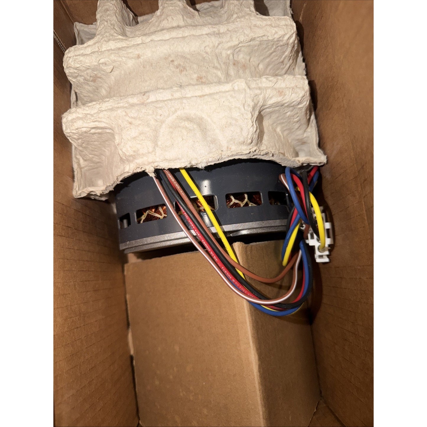 Electric motor with exposed copper windings and multiple colored power and control wires, partially protected by molded pulp packaging inside a cardboard box.