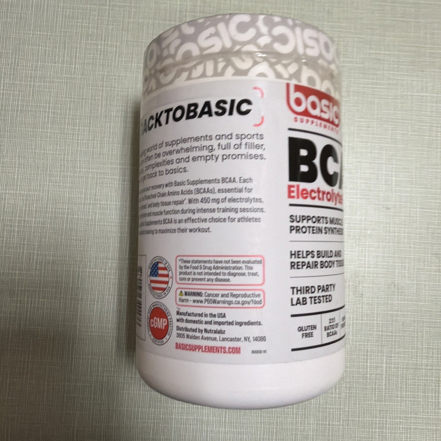 White supplement container with red and black text displaying product benefits for muscle support and protein synthesis, third-party lab testing, gluten-free and batch-tested labels, along with manufacturing and safety information on the side.