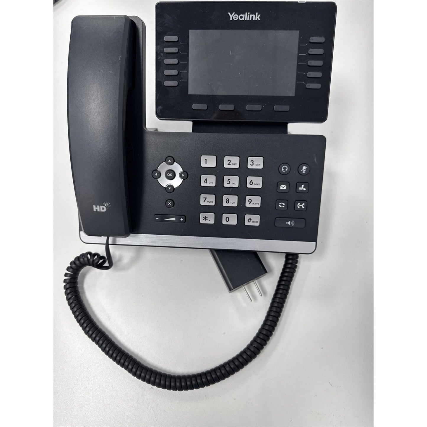 Black Yealink office desk phone featuring a large screen, multiple function buttons, numeric keypad, and a coiled handset cord on a white surface.