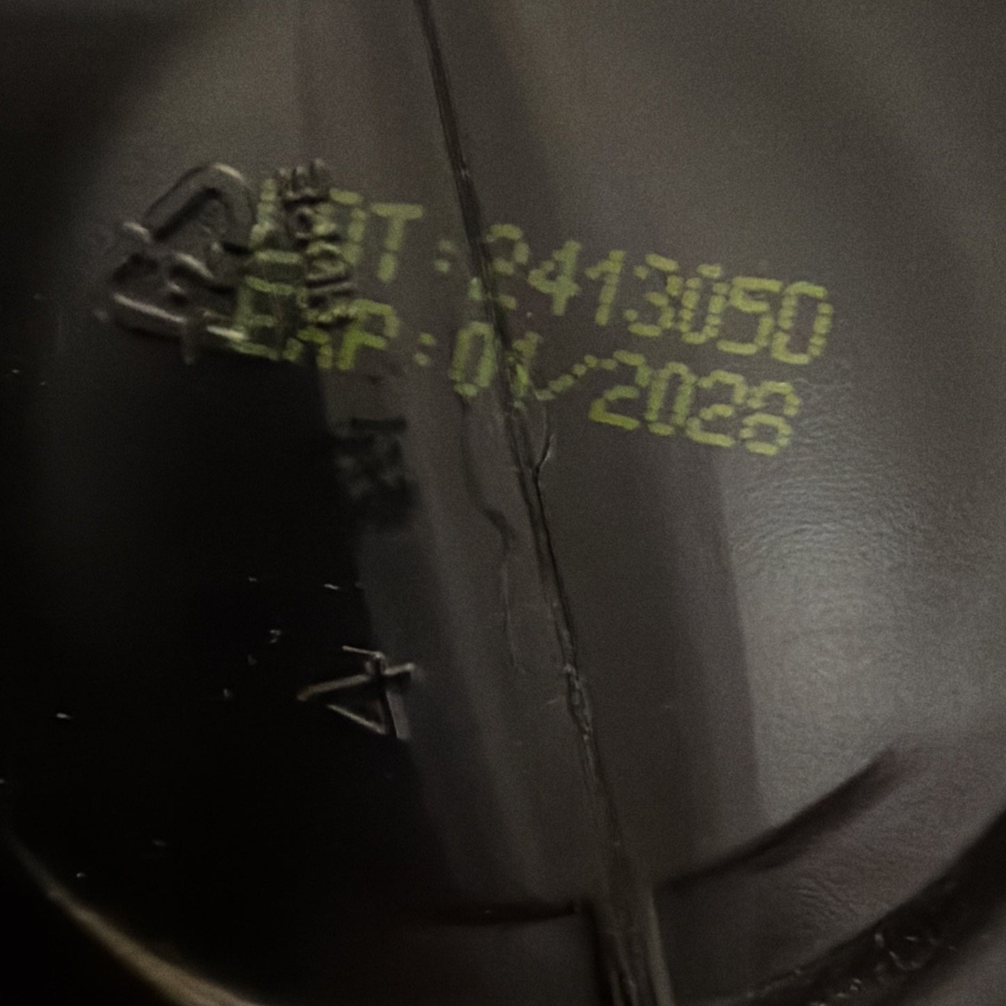Close-up of a black plastic surface with yellow printed batch number "2413090" and expiration date "01/2028" on a textured background.