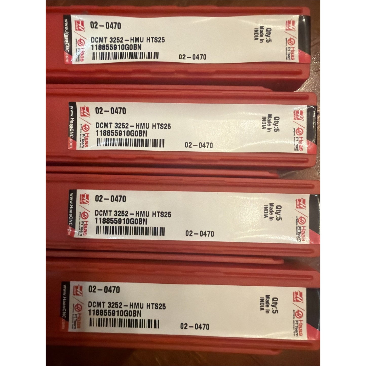 Stack of four red rectangular plastic cases with white labels displaying product codes "DCMT 3252 - HMU HTS25," barcodes, and text including "Made in India" and "02-0470" on each label.