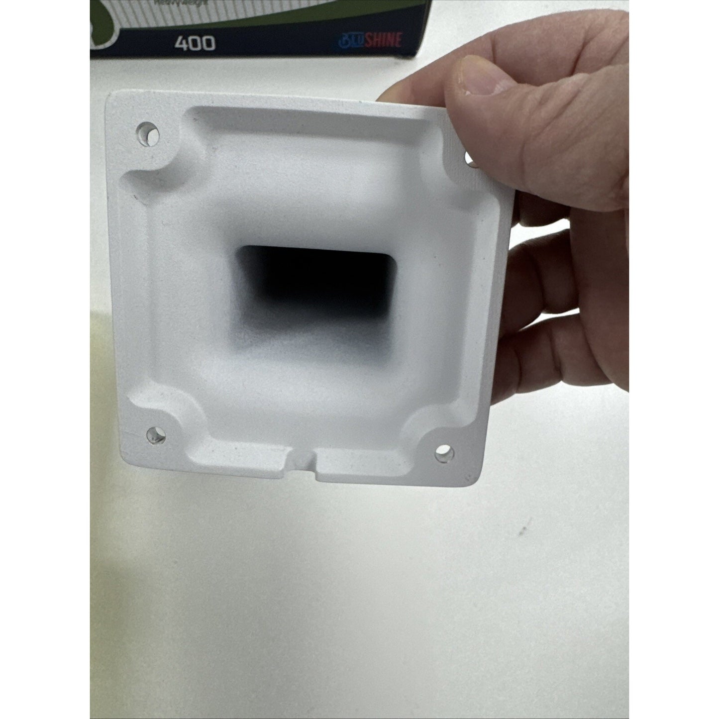 Hand holding white Cisco Meraki MA-MNT-MV-30 security camera accessory mount showing four mounting holes and square cavity