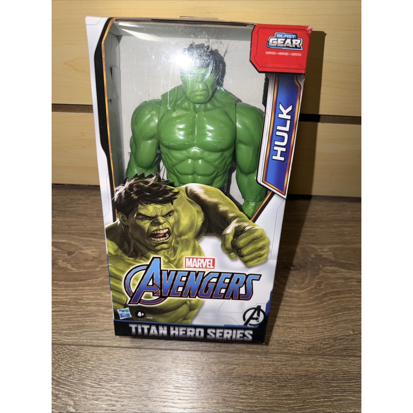 Green Hulk action figure with muscular build, displayed inside a clear-front box featuring Marvel Avengers branding and "Titan Hero Series" label on a wooden surface.