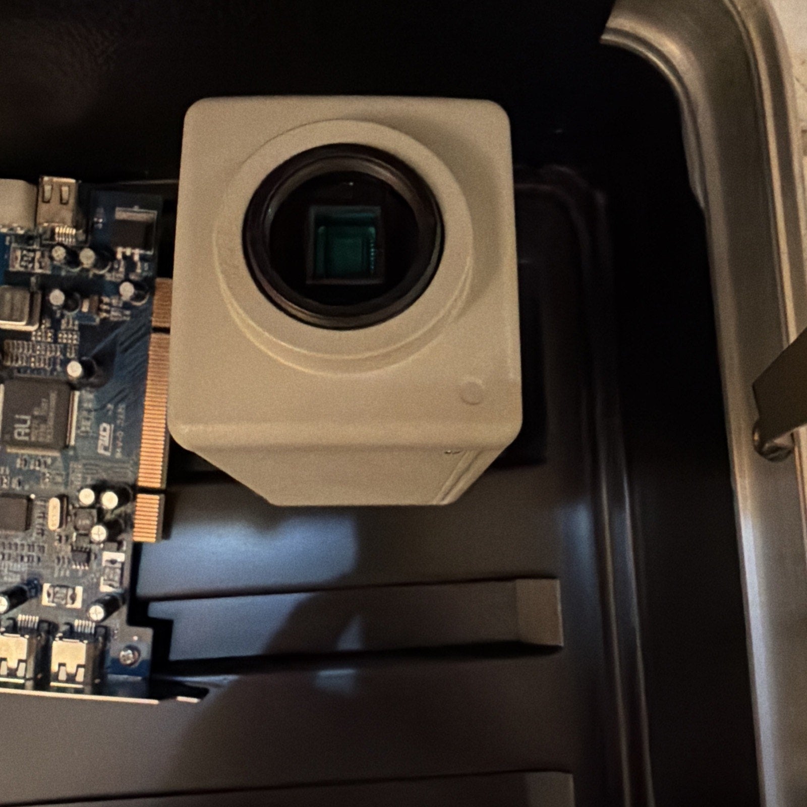 Close-up of a white digital camera sensor module attached to a blue circuit board inside a black electronic device casing.