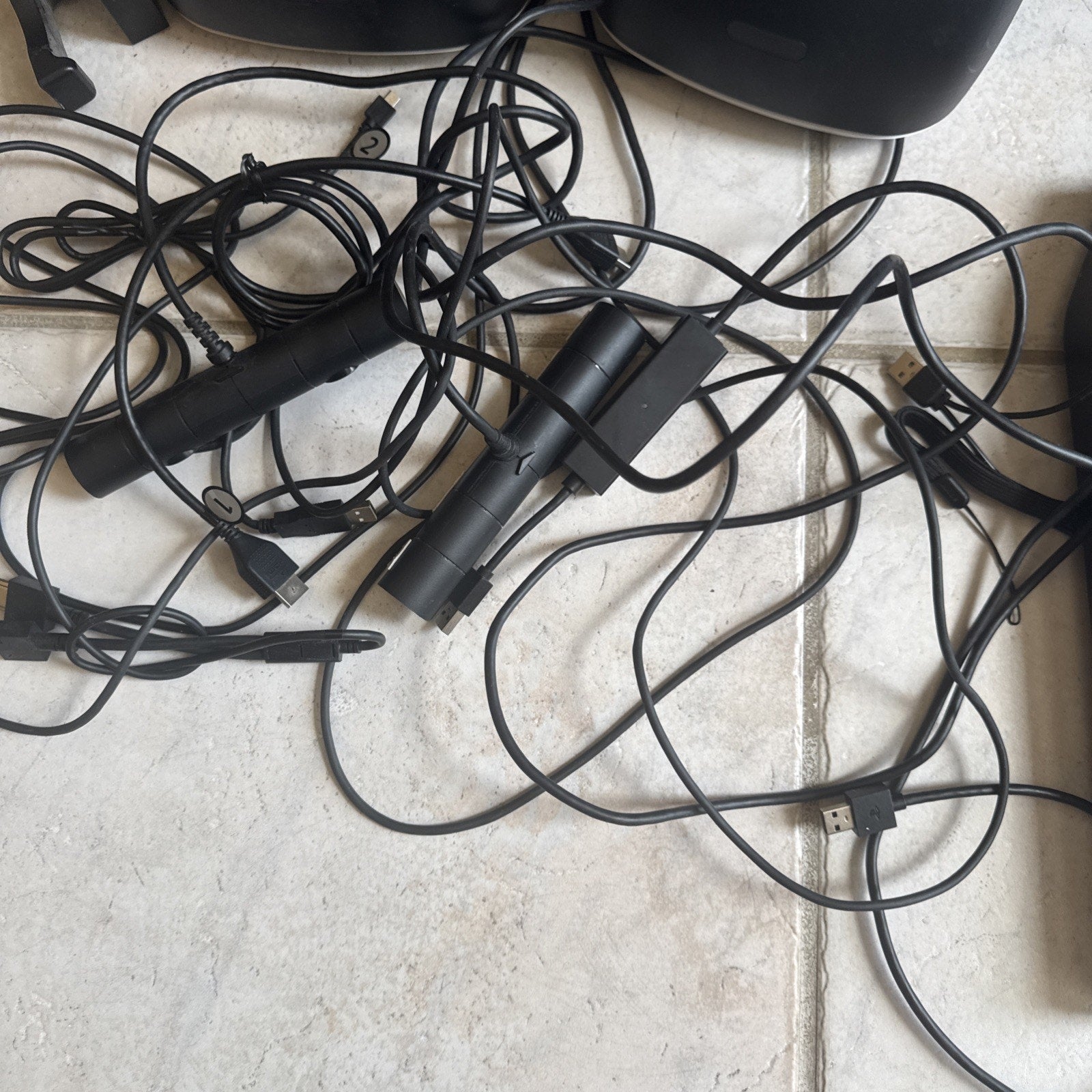 Two PlayStation VR sensor bars and assorted USB and HDMI cables tangled on tiled floor with headset partial view