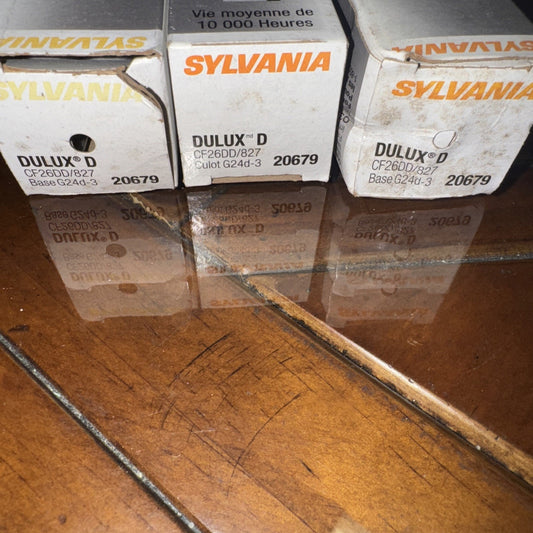 Three Sylvania Dulux D 26 watt compact fluorescent light bulb boxes on wooden floor with reflection visible