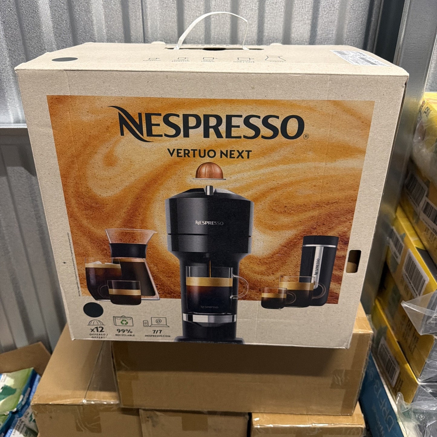Nespresso Vertuo Next coffee machine in black displayed on packaging with images of brewed coffee cups, eco-friendly icons, and product features on a cardboard box.