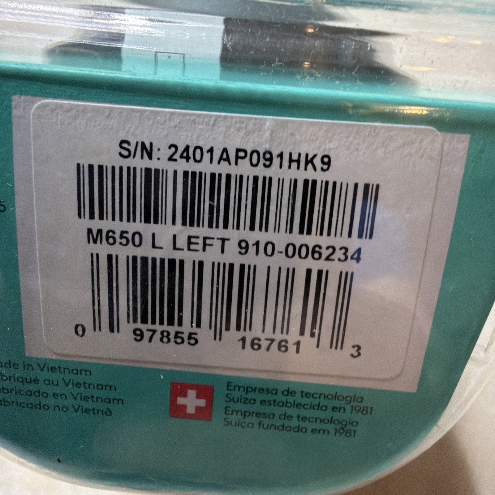 Close-up of a product barcode label showing serial number, model number M650 L LEFT, and origin information indicating manufacturing in Vietnam with a Swiss technology emblem and multilingual text.
