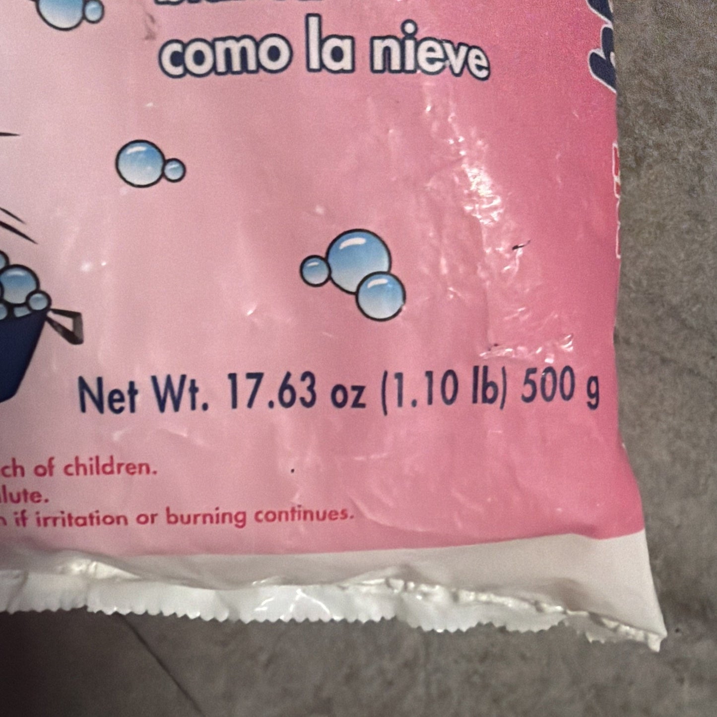 Close-up of a pink plastic package showing net weight information as 17.63 oz (1.10 lb) 500 g with small blue bubble illustrations above a white tear strip at the bottom edge.