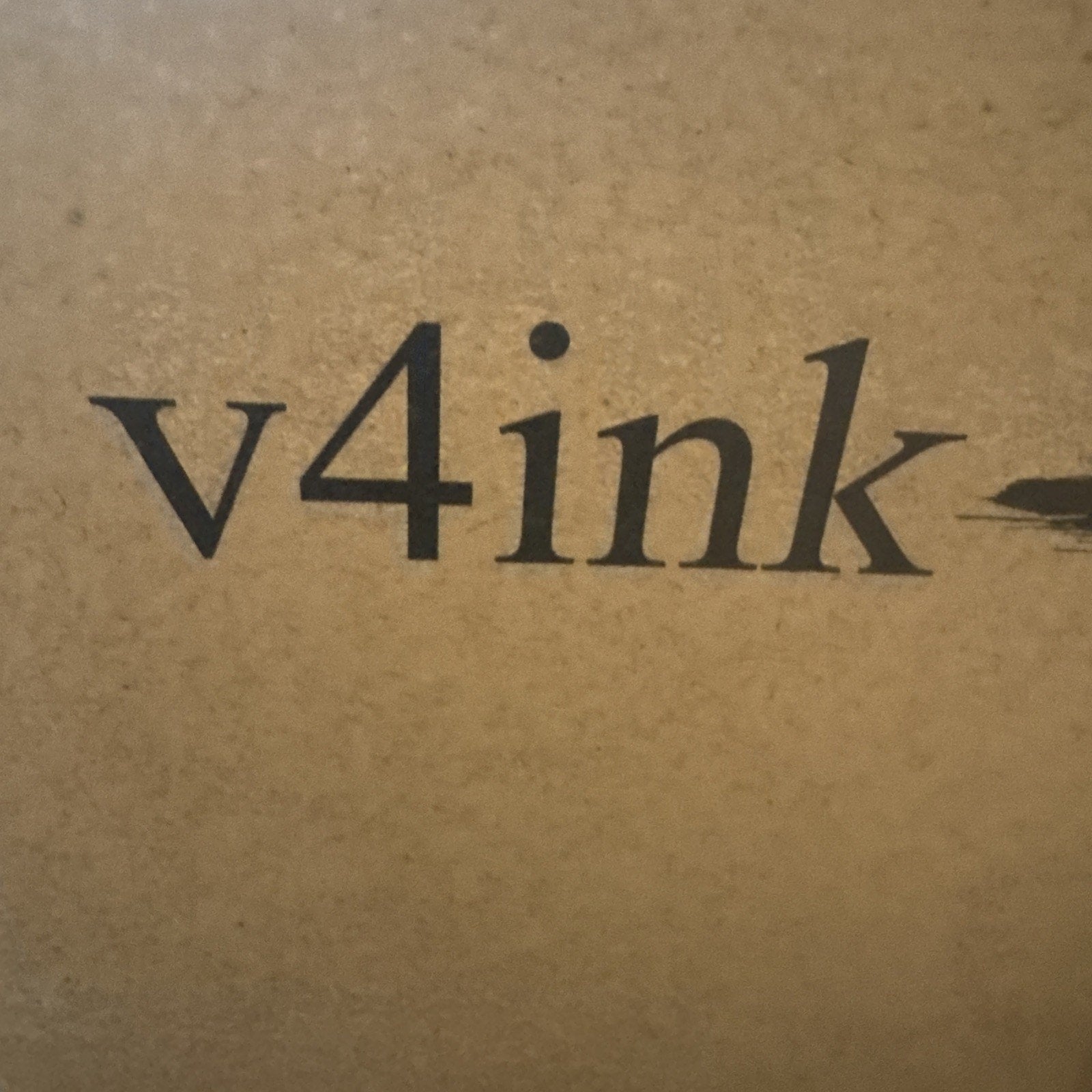 Close-up of black printed text "v4ink" on a textured brown cardboard surface.