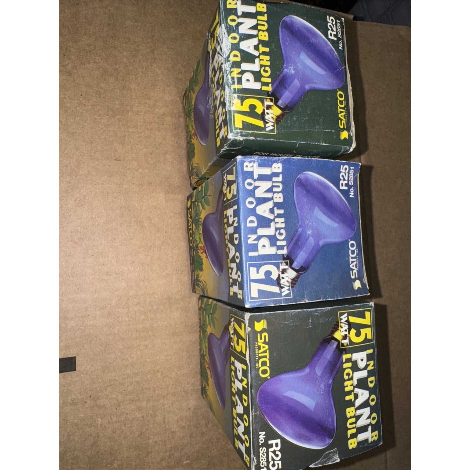 Three Satco S2851 blue 75 watt R25 medium base indoor plant light bulbs in original packaging stacked on cardboard surface