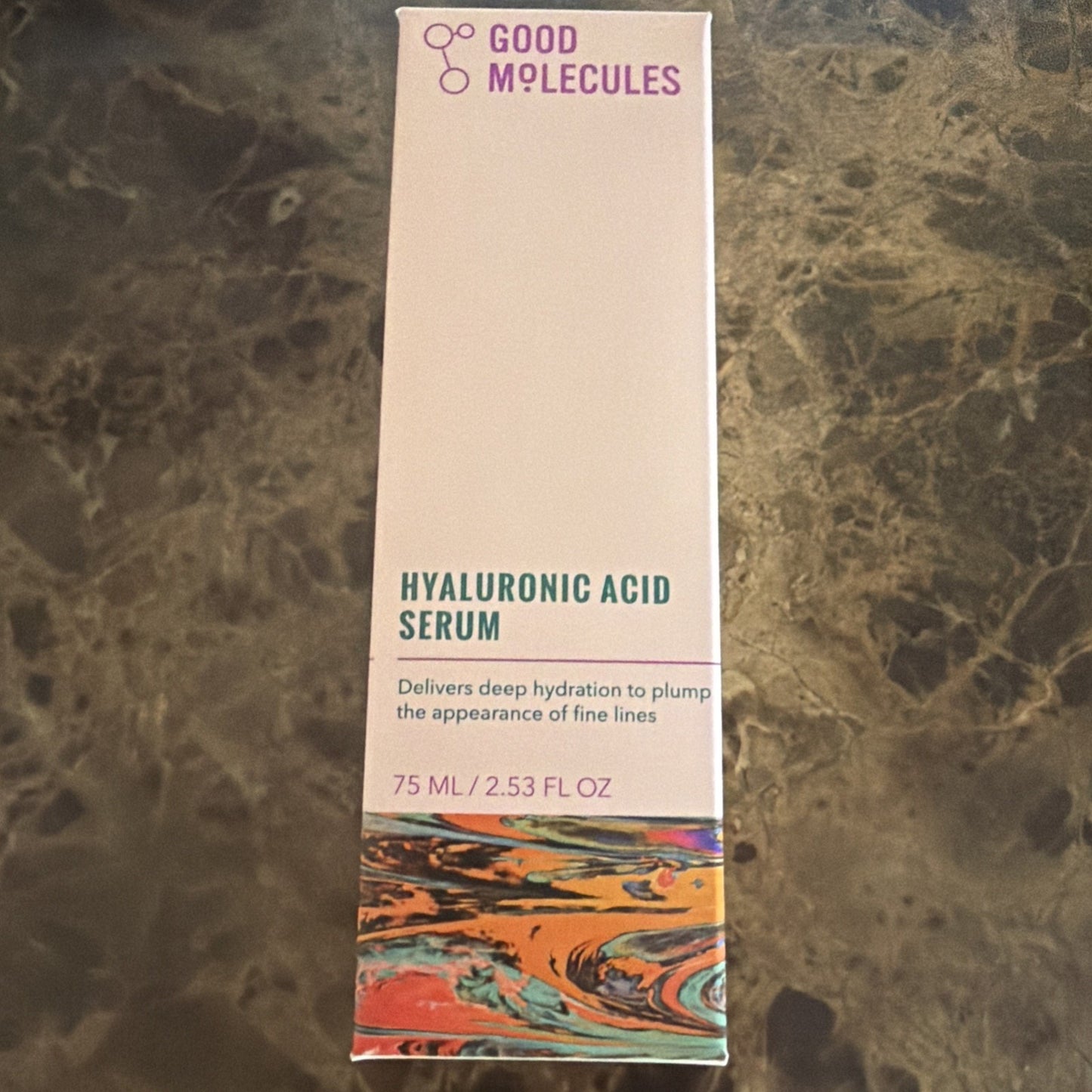 Tall rectangular box of Good Molecules Hyaluronic Acid Serum with a white background, minimalist purple and teal text, and a colorful marbled pattern at the bottom edge.