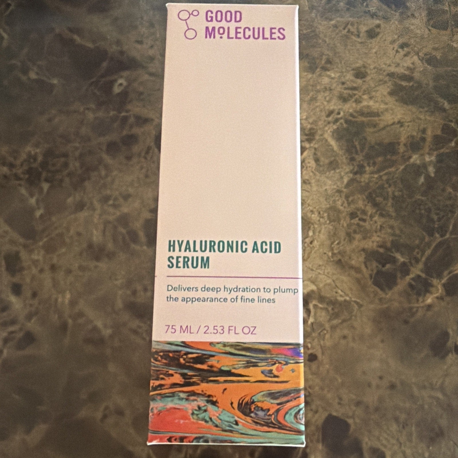 Tall rectangular box of Good Molecules Hyaluronic Acid Serum with a white background, minimalist purple and teal text, and a colorful marbled pattern at the bottom edge.