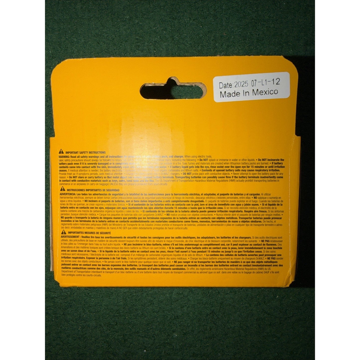 Yellow rectangular product backing with safety instructions and warnings printed in multiple languages, featuring a white sticker labeled "Date 2025 07-11-12 Made in Mexico," placed on a dark green textured surface.