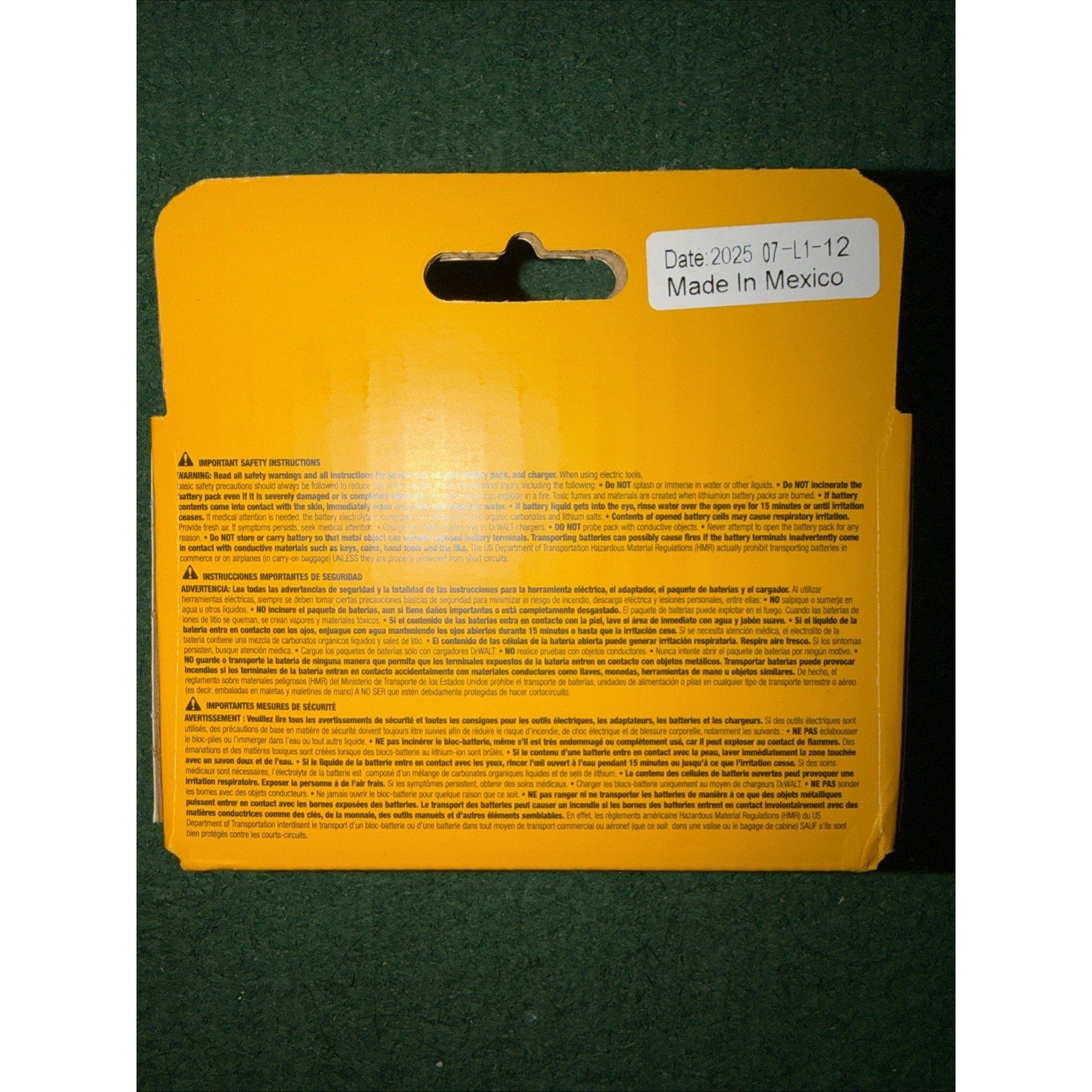 Yellow rectangular product backing with safety instructions and warnings printed in multiple languages, featuring a white sticker labeled "Date 2025 07-11-12 Made in Mexico," placed on a dark green textured surface.