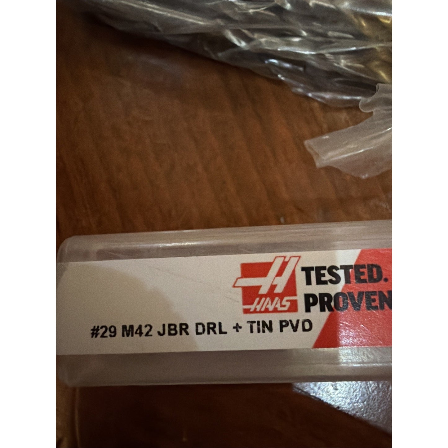 Close-up of a plastic tool case label on a wooden surface displaying "#29 M42 JBR DRL + TIN PVD" along with a red and black Haas logo and text reading "TESTED. PROVEN.