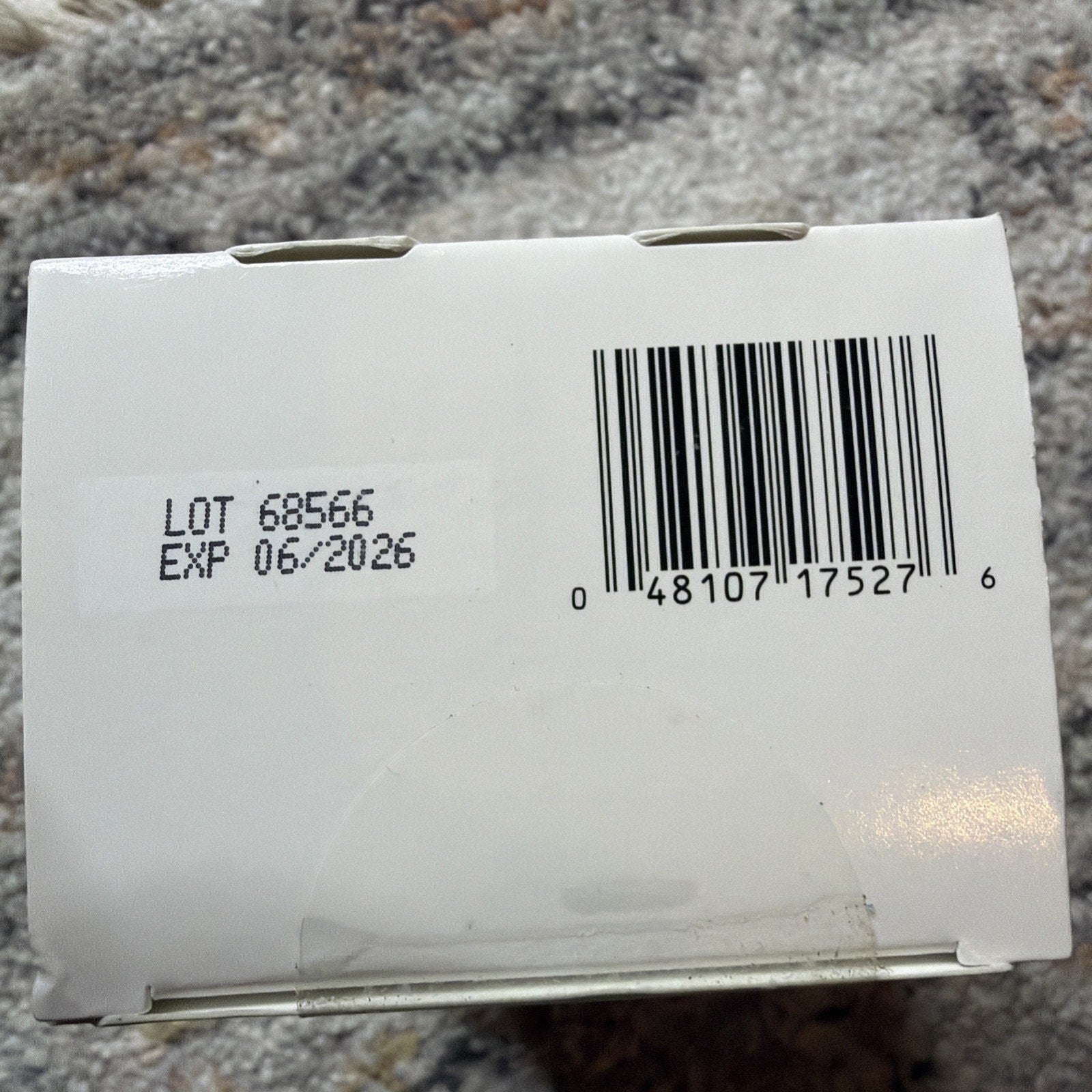 White product box showing a barcode and a printed label with lot number 68566 and expiration date of June 2026 on a textured surface.