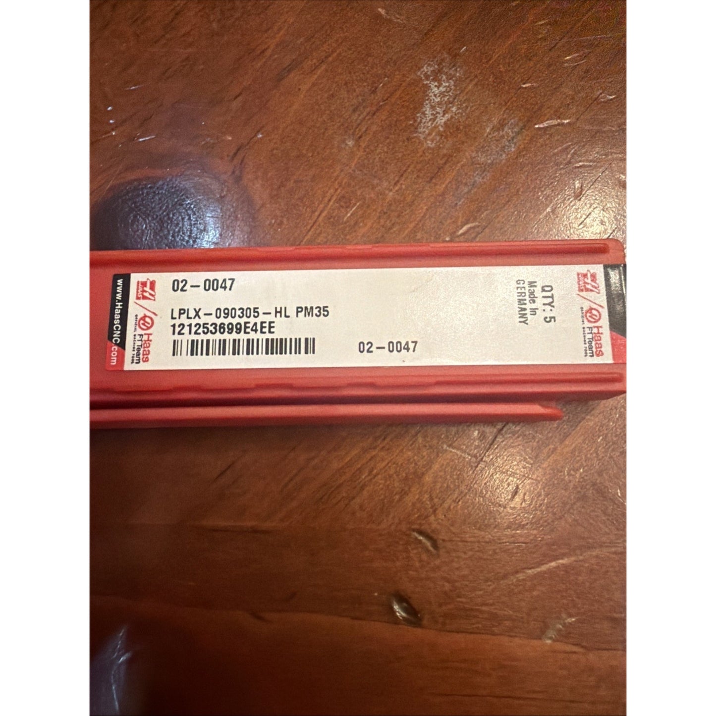 Red rectangular plastic case with a white label displaying product code "LPLX-090305-HL PM35," barcode, quantity "Qty. 5," and "Made in Germany," placed on a wooden surface.