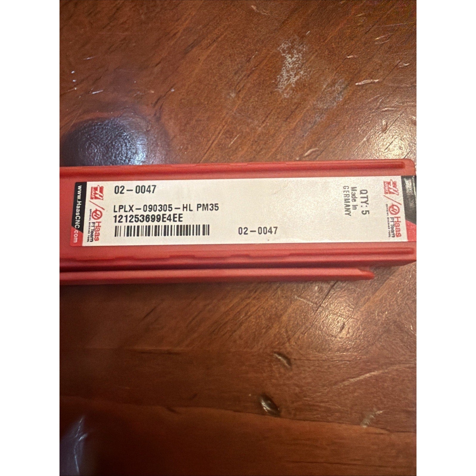 Red rectangular plastic case with a white label displaying product code "LPLX-090305-HL PM35," barcode, quantity "Qty. 5," and "Made in Germany," placed on a wooden surface.