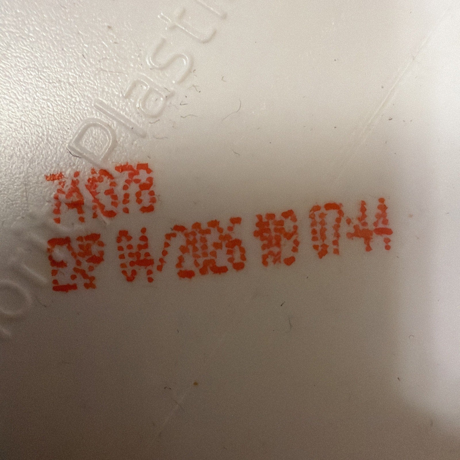 Close-up of a white plastic surface with red printed code and expiration date reading "EXP W/026 BD 074" next to embossed text partially visible in the background.