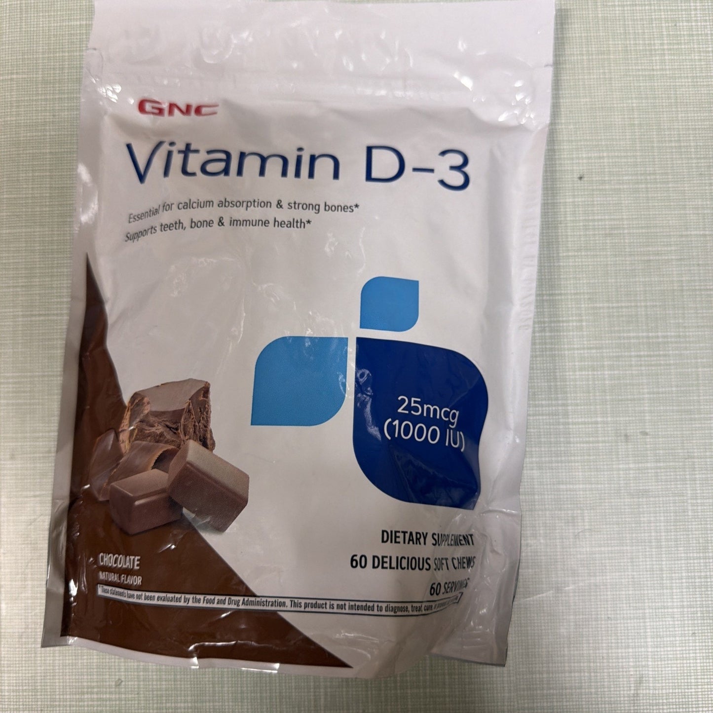 White and brown resealable pouch of Vitamin D-3 dietary supplement featuring chocolate-flavored soft chews with dosage information of 25 mcg (1000 IU) and health benefit claims.