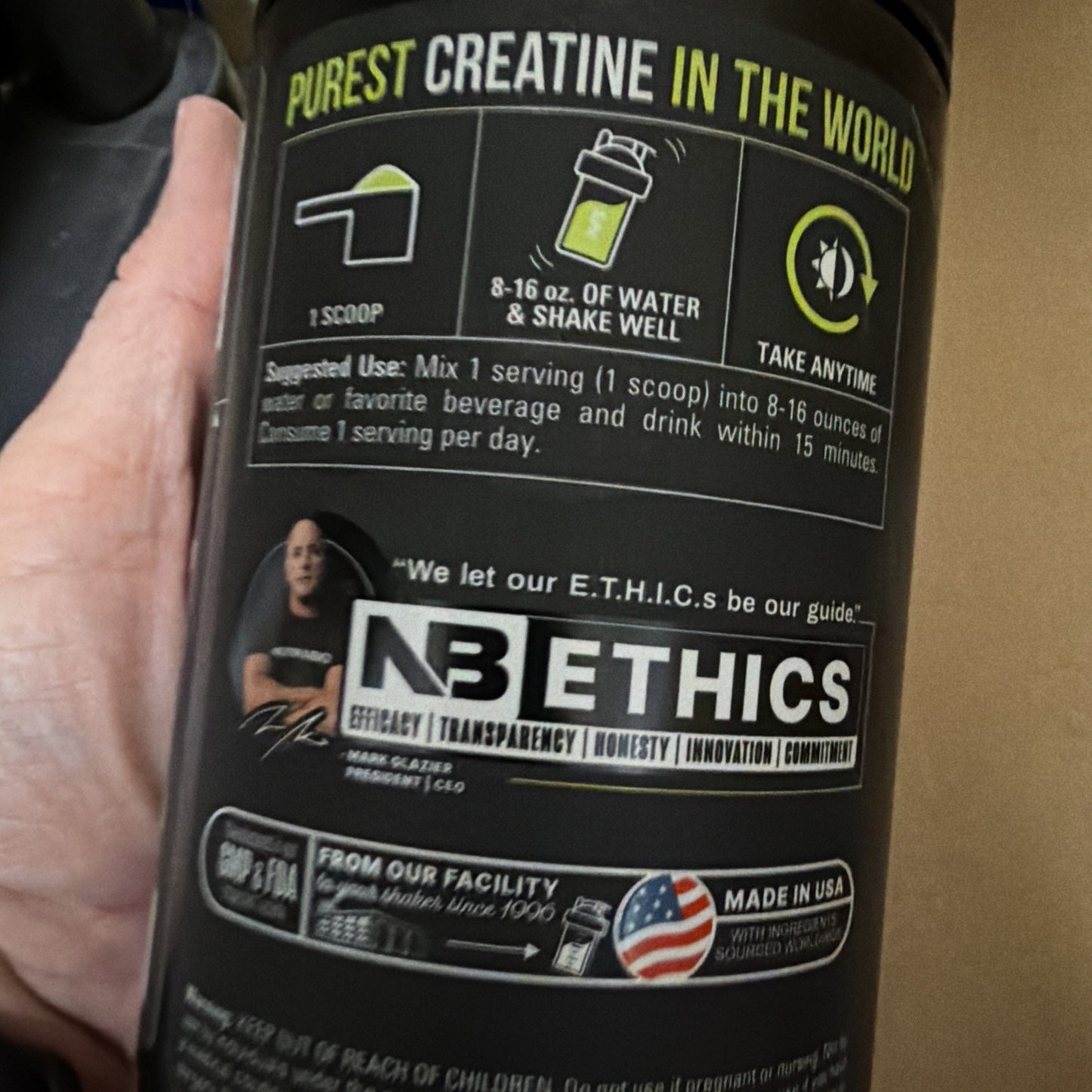 Close-up of a black supplement container label showing directions to mix one scoop with 8-16 ounces of water, branding for NB Ethics highlighting core values, and a Made in USA emblem.