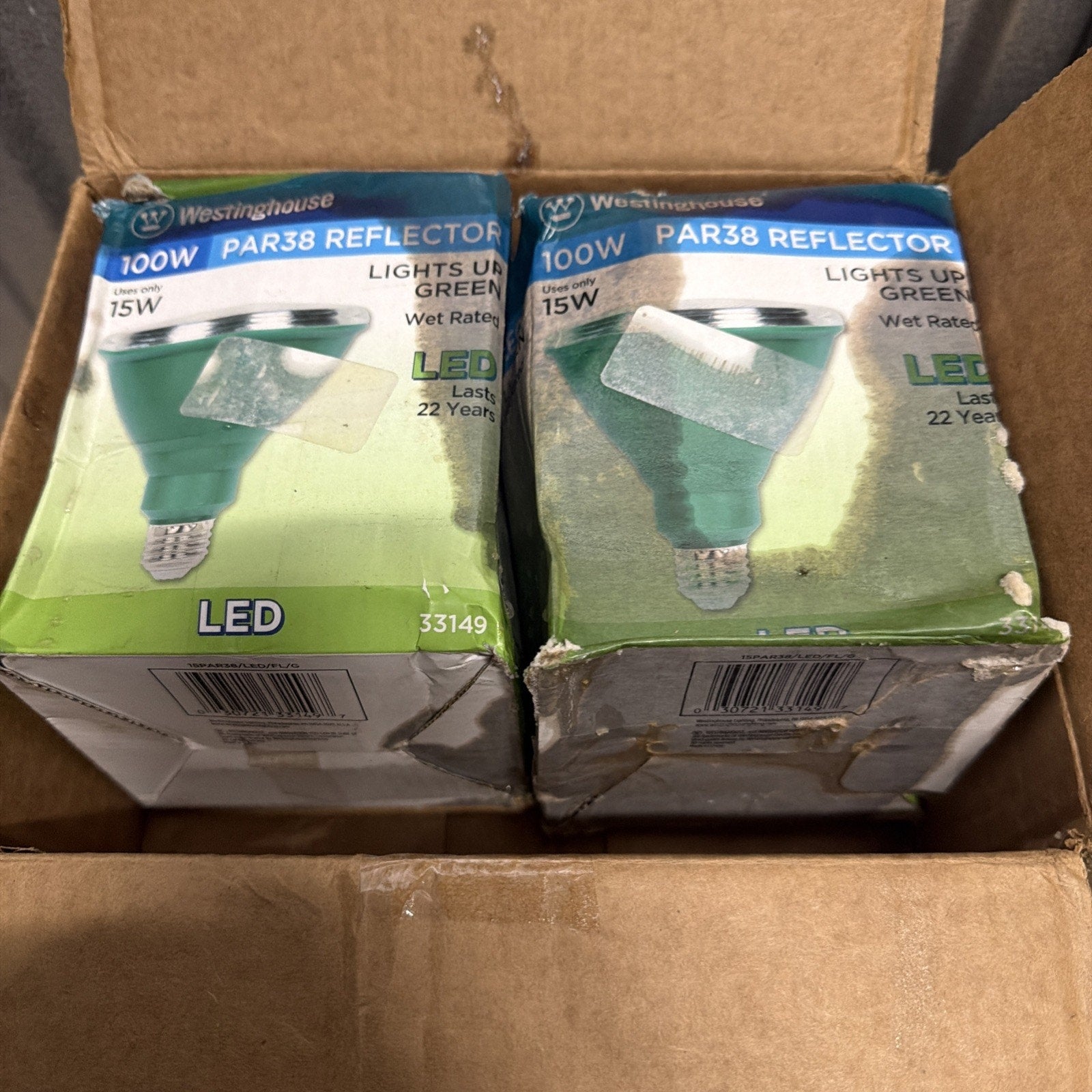 Two worn green and silver LED PAR38 reflector light bulb boxes inside a larger cardboard shipping container, showing product details for 100W equivalent, 15W bulbs.